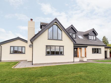A house with multiple windows a chimney and a tiled roof with dormer windows and a grassy lawn at Tara Spa in Trelawnyd