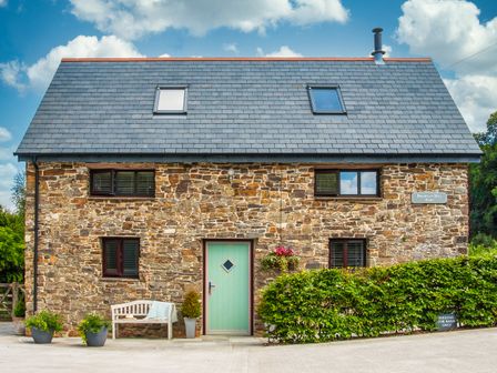 A stone house with a green door bench and plants outside at Brightley Mill Barn Brightley near Okehampton