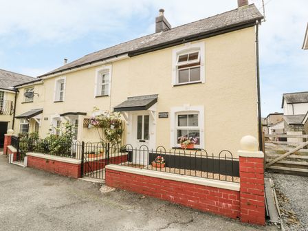A yellow cottage with white framed windows and a small garden area at Brickfield Cottage in Machynlleth