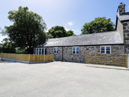 An exterior view of a stone house with a slate roof fenced area and wooden gate at Cefn Bryn Bach in Criccieth