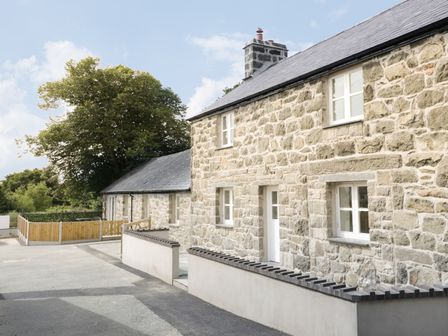 A stone house with white framed windows and a wooden fence outside surrounded by trees at Cefn Bryn Mawr in Criccieth
