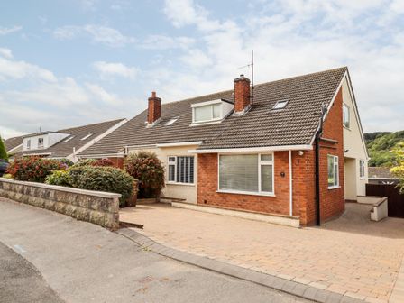 A semi detached house with driveway and shrubs along a stone wall at 4 Bodnant Road in Rhos On Sea