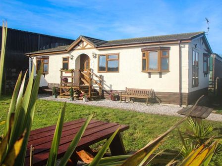A single story house with wooden windows and a small porch with steps in front and outdoor benches at The Dovecote in Hartland
