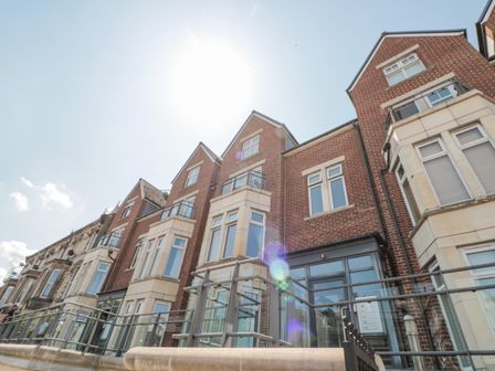 View of a row of brick townhouses with glass balcony railings under a clear sky at Harbour Lodge in Whitby