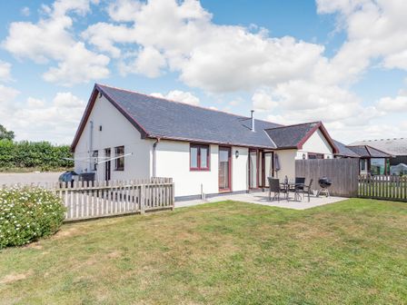 A house with a fenced yard a patio with a table chairs and a barbecue at Elworthy View Bishops Nympton near South Molton