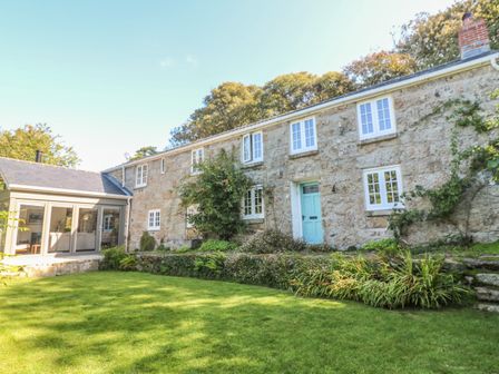 A stone house with white windows blue door and green lawn at Ros Vale in St Buryan