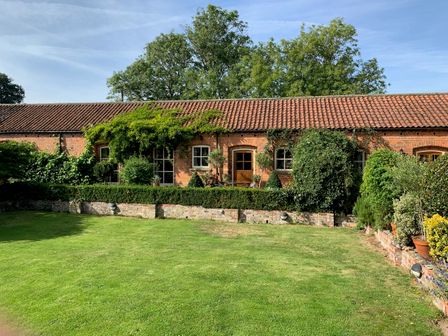 A lawn garden with shrubs and brick wall in front of a brick house with tiled roof at Stable Cottage in Withernwick near Hornsea