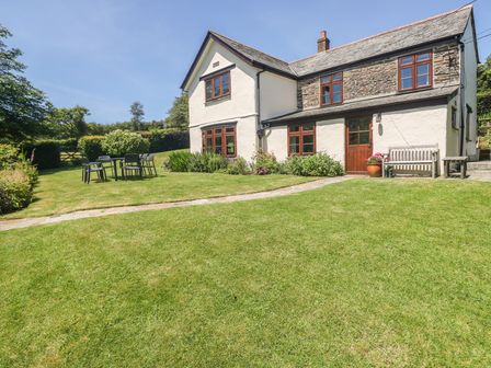 A stone and white plaster house with wooden framed windows and a garden with outdoor table and chairs at Meadow Lea in Pensilva near Liskeard