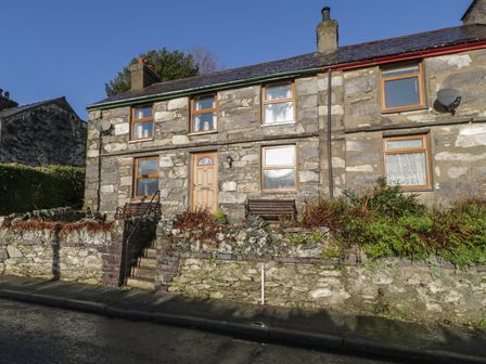 A stone house with wooden framed windows and a front door with stairs and benches at 60 Hyfrydle Road in Talysarn near Caernarfon