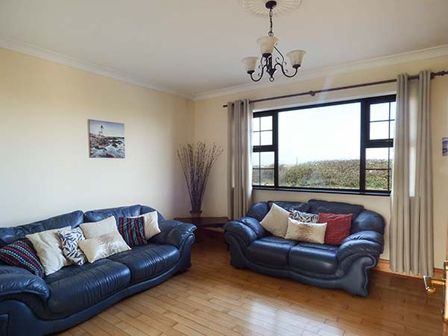 A living room with two blue leather sofas and cushions window and curtains on wooden floor at Flynns Cottage in Quilty County Clare