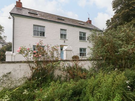 A white two-story house with blue windows and door surrounded by greenery and flowers at Ty Llwyd Nevern near Cardigan