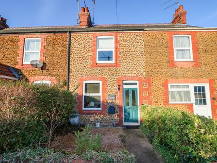 A stone and brick terraced house with a green front door and shrubbery in front at Carrstone Cottage in Heacham