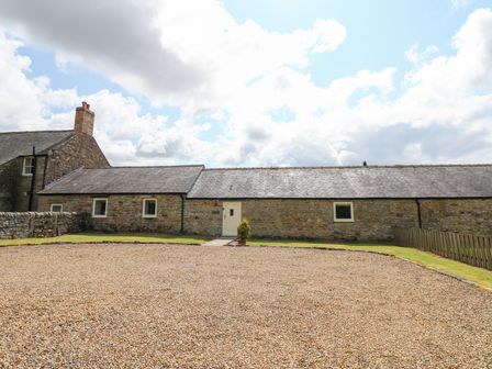 A stone cottage with a gravel driveway and a small plant at Shepherds Burn Cottage Bellingham