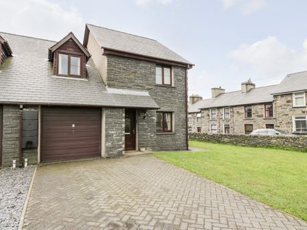 A driveway leading to a garage and entrance of a stone house with a lawn at 6 Stad Yr Ysgol in Manod near Blaenau Ffestiniog