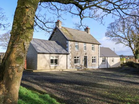 A two-story house with a gravel driveway and leafless trees in front at Rosies Cottage in Bushmills County Antrim