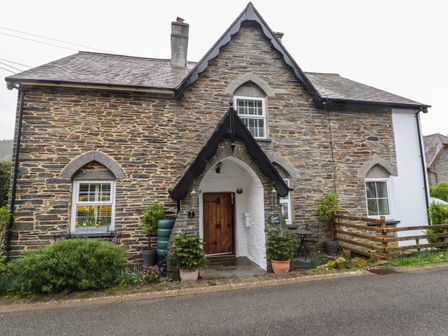 Stone cottage with arched doorway and wooden door with potted plants outside at Siskin in Dinas Mawddwy near Dolgellau