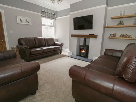 A living room with three brown leather sofas a wood stove under a wall mounted TV and wooden shelves on the wall at Dumbuie in Haltwhistle