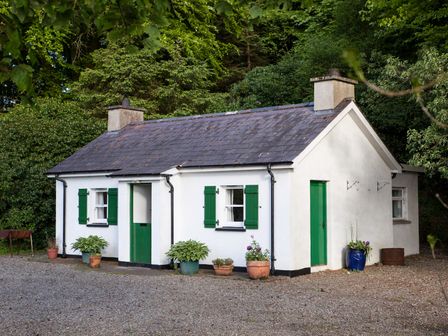 A small white cottage with green doors and window shutters surrounded by plants at Mr McGregors Cottage in Gortin County Tyrone
