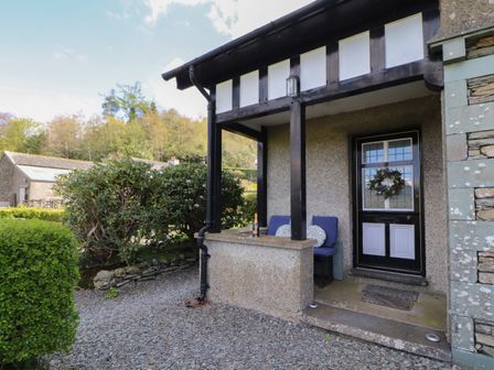 A small porch with two blue chairs and pillows next to a black and white front door with a wreath at Glenside in Far Sawrey