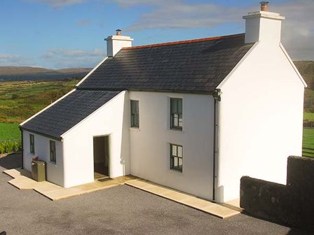 A white farmhouse with black roof and chimneys in a rural landscape at Nellies Farmhouse in Durrus near Bantry County Cork
