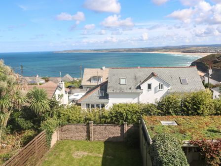 A backyard with a lawn and hedges with houses and the ocean in the background at Seafield in Carbis Bay near St Ives