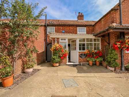 A brick house entrance with potted plants and flowers around at Six Dovehouse Row in Swaffham