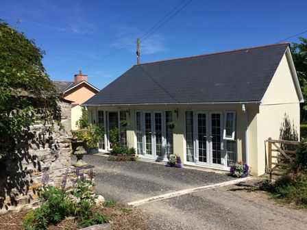 A small pale yellow building with multiple white framed glass doors and flower pots outside near a gravel driveway