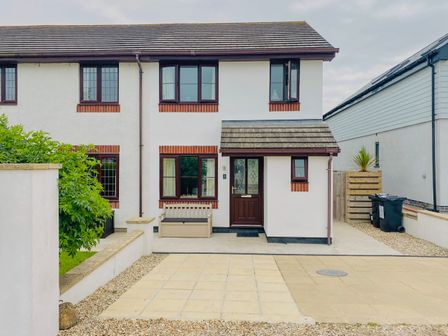 The front exterior of a semi detached house with a brown door and windows a bench outside and paved driveway at 7 Harlyn Cottages Harlyn Bay near Padstow