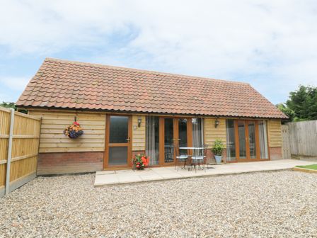 A single story house with tiled roof wooden walls patio area with table and chairs and gravel in front at Foxley Wood Cottage in Spixworth
