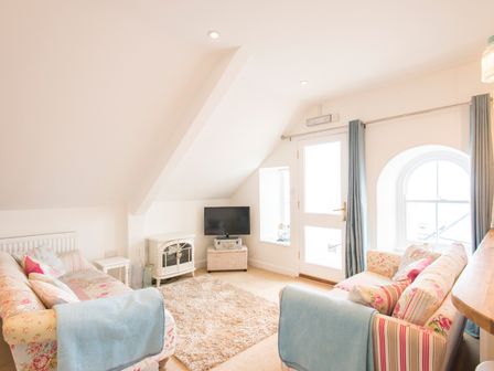 A living room with two floral sofas a rug a small TV and light blue curtains at Spiral View in Perranporth