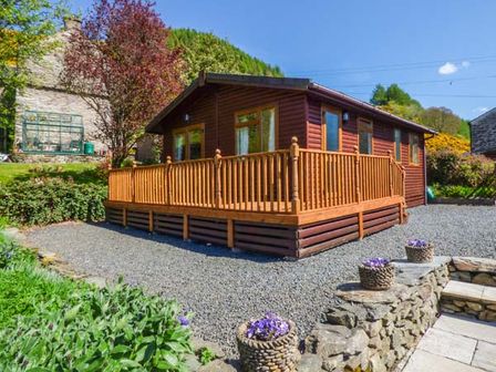 A wooden cabin with a raised deck and potted flowers on a stone wall at North Lodge in Kendal