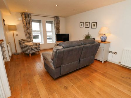 A living room with a gray couch and patterned armchair facing a television near windows at 6 Mill Wharf in Berwick-upon-Tweed