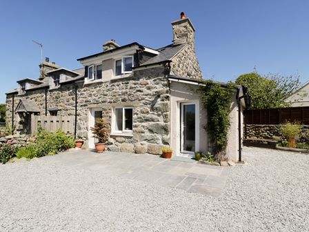 An exterior view of a stone cottage with a gravel driveway and potted plants at 2 Borthwen Cottages in Dyffryn Ardudwy