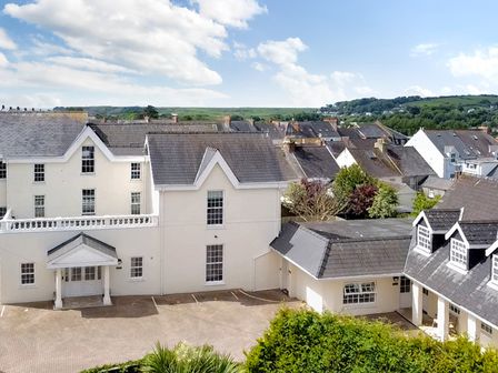 A white residential building with pitched roofs and parking spaces with multiple houses and greenery in the background at South Beach at The Hideaway in Tenby