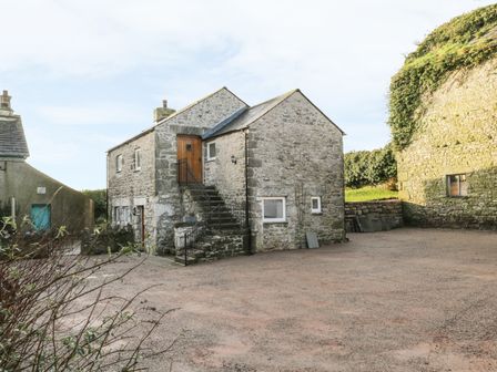 A stone building with an external staircase and gravel courtyard at The Granary Loft in Bardsea
