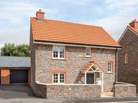 A stone house with a red tiled roof and a garage next to it at Tus Nua Cottage in Carhampton