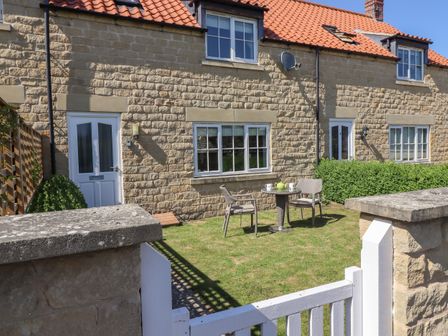 A stone house with a tiled roof and a small garden with a table and two chairs at 8 Pottergate Mews in Helmsley