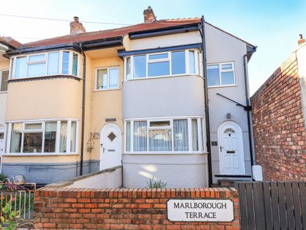 A street view of terraced houses with bay windows and front doors behind a brick wall at No 1 Kelly Cottages in Scarborough