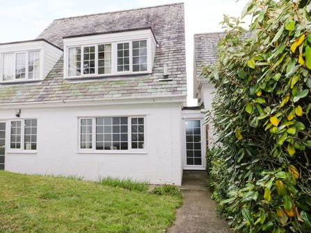 The exterior of a white house with multiple windows a tiled roof a grass lawn and a paved walkway beside bushes at The Cottage at Wylan Hall in Beaumaris