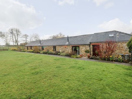 A stone building with a slate roof and a large green lawn in front at The Barn at Harrolds Farm Kilgetty