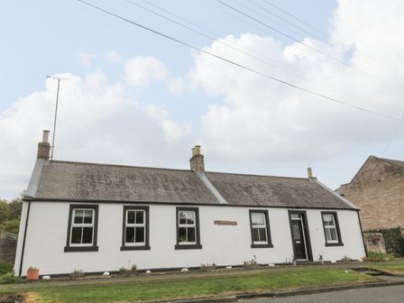A single story white cottage with five windows and a black door at Victoria Cottage in Norham