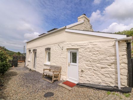 Exterior of a stone cottage with a white door wooden bench and gravel pathway at Taliharris Cottage in Llandysul