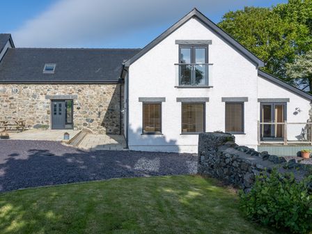 A house with white and stone exterior walls surrounded by grass trees and a stone wall at Sgubor in Pentraeth