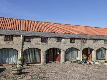 A stone building with arched doorways and a tiled roof with cobblestone ground at The Mistal in Glanton near Alnwick