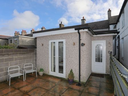 A small back patio with two chairs and potted plants outside a building with a white door and glass double doors at The Studio @ The Old Post Office in Cemaes Bay