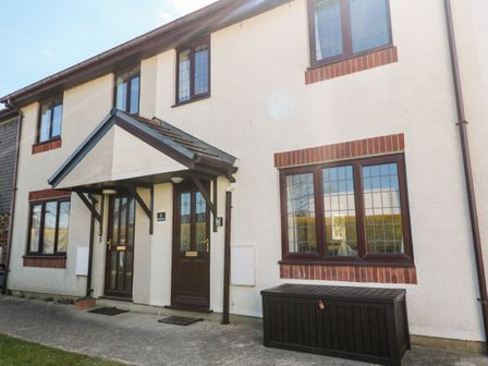 The exterior of two attached houses with brown doors and windows and a small porch at Rockpool in Harlyn Bay near St Merryn