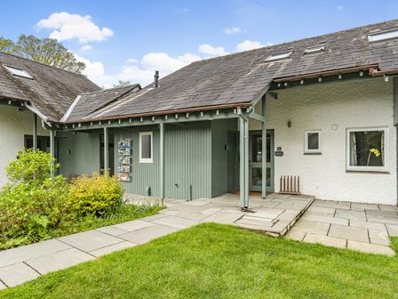 An exterior view of a cottage with green door and siding a stone walkway and grass at Rowan - Woodland Cottages in Windermere