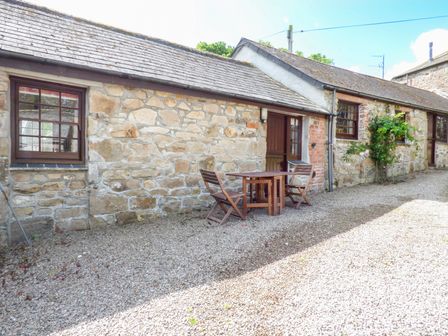 A stone cottage exterior with wooden windows a door and a wooden table and chairs on a gravel driveway at The Bullshed in Marazion