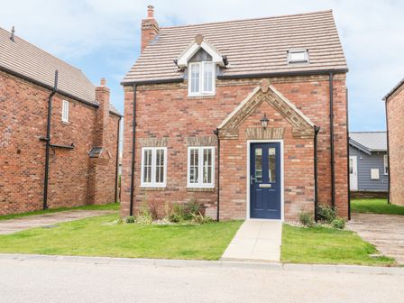 A brick house with a blue door and three windows and a small lawn at Flip Flops The Bay near Filey