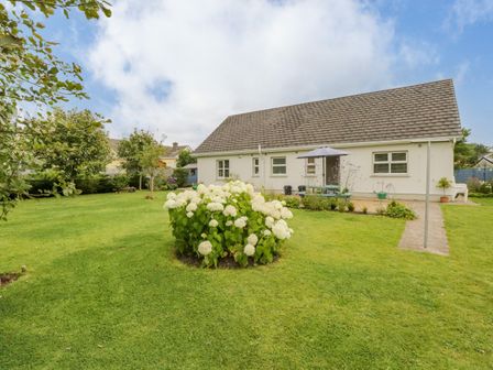A large lawn with flower bushes and trees in front of a single story house with a gable roof at 2 Castle Cove in Dromahair County Leitrim
